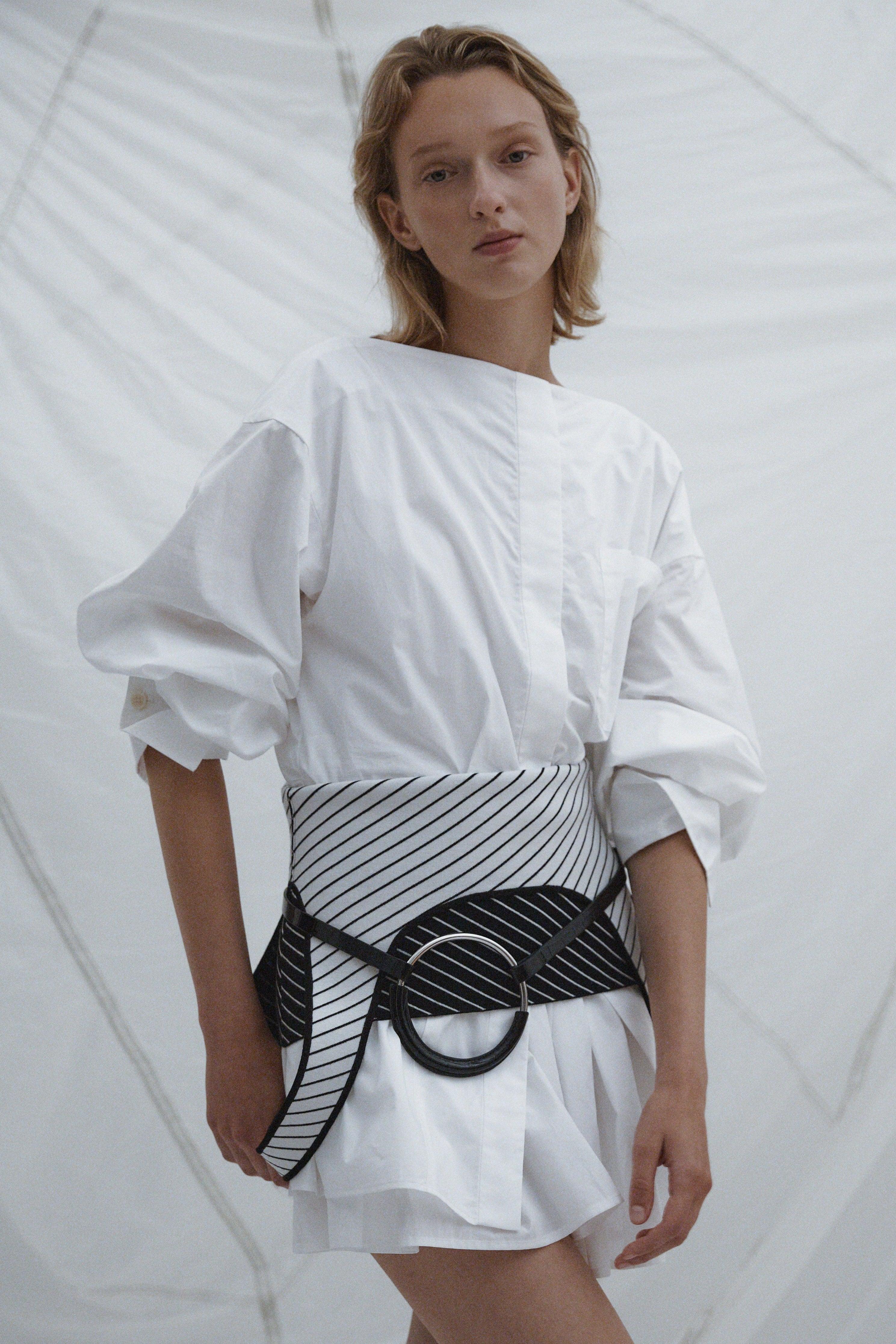 Woman wearing a white cotton dress with a wrapped metal belt worn over black and white belt.