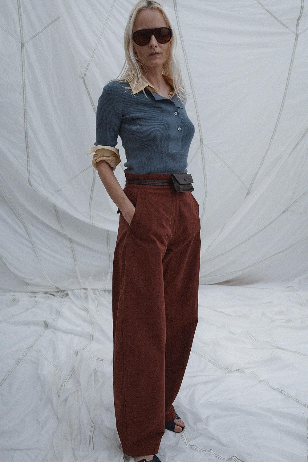 Person wearing a blue top and brown pants against a white textured backdrop